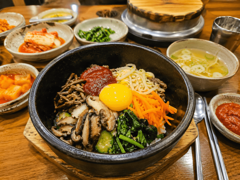 Bibimbap Korean Set Meal Bibimbap in a hot stone bowl with vegetables, egg yolk, gochujang, soup, kimchi, and Korean side dishes