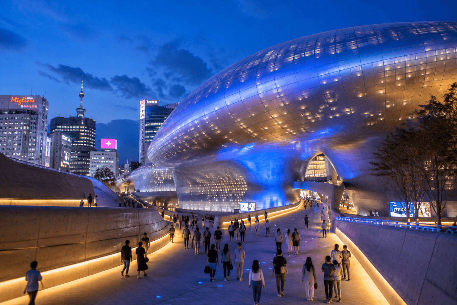 Dongdaemun Design Plaza in Seoul at night with travelers walking through the illuminated plaza