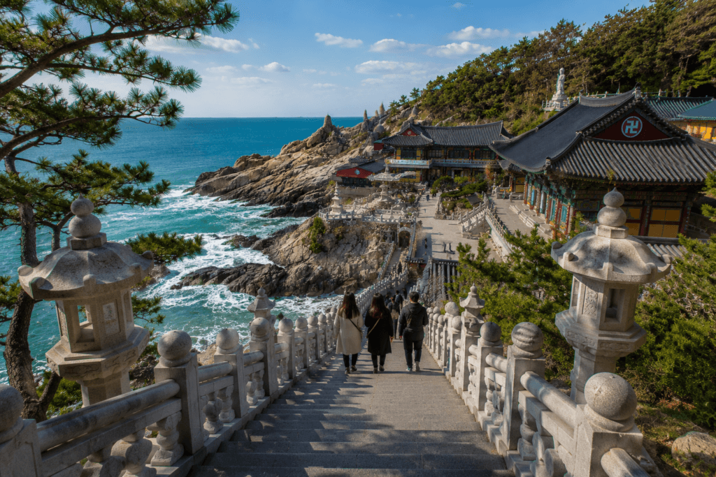 Stone staircase leading down to Haedong Yonggungsa Temple with ocean views, pine trees, and traditional temple buildings