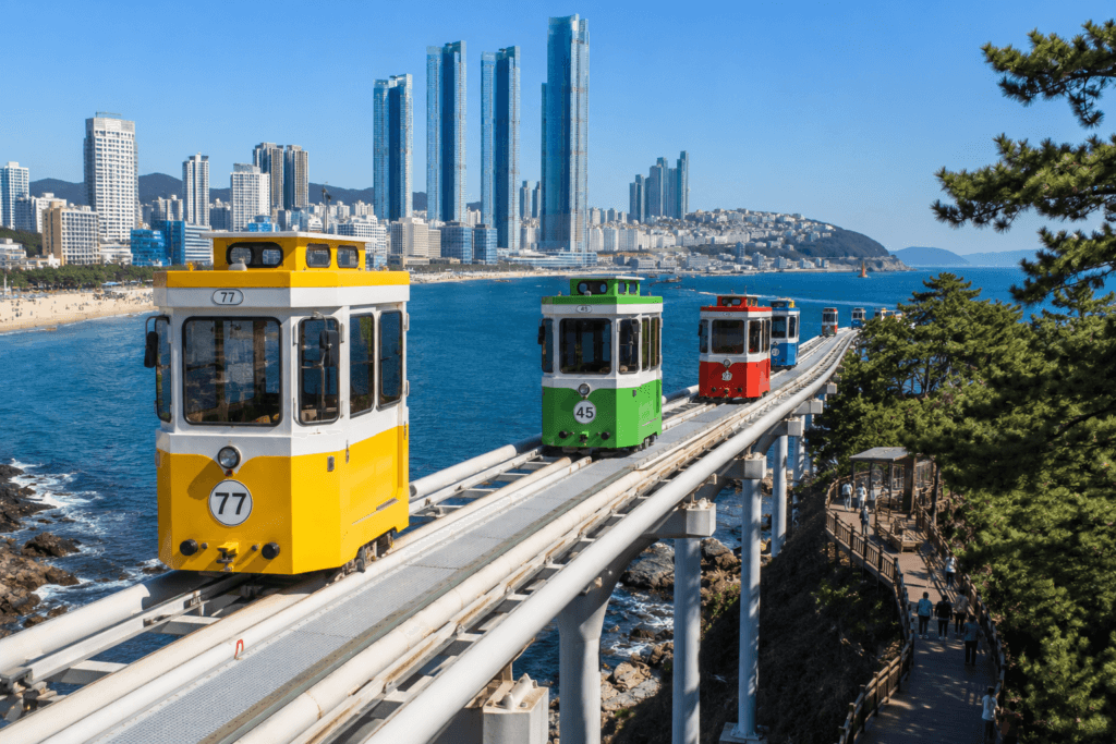 Colorful Haeundae Sky Capsule cars traveling along the coastal rail with ocean and Busan skyline views