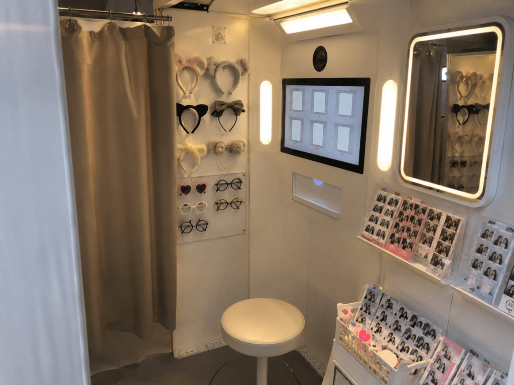 Inside a Korean four-cut photo booth with curtain, mirror, props, frame selection screen and printed photo strips