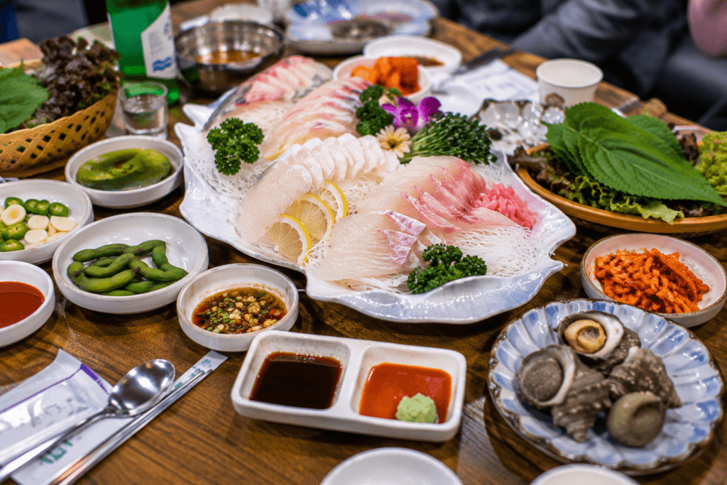 Korean sashimi table in Busan with sliced hoe, leafy wraps, sauces, banchan, and seafood side dishes