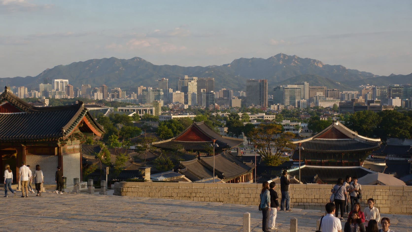 Traditional palace rooftops, modern Seoul skyline, and mountains viewed in warm afternoon light