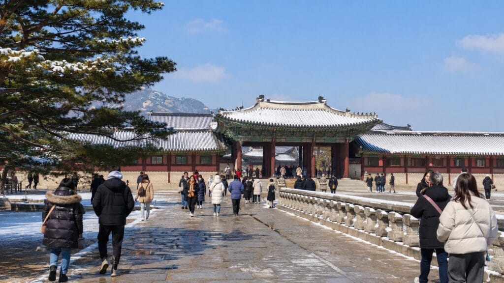 Visitors wearing winter coats at a snow-covered royal palace in Seoul