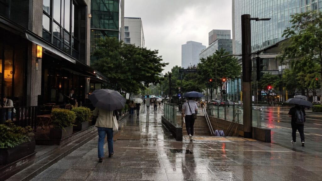 People carrying umbrellas on a wet Seoul street during the rainy season