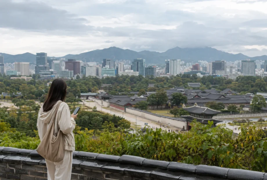 Traveler checking the weather above palace rooftops and the Seoul skyline
