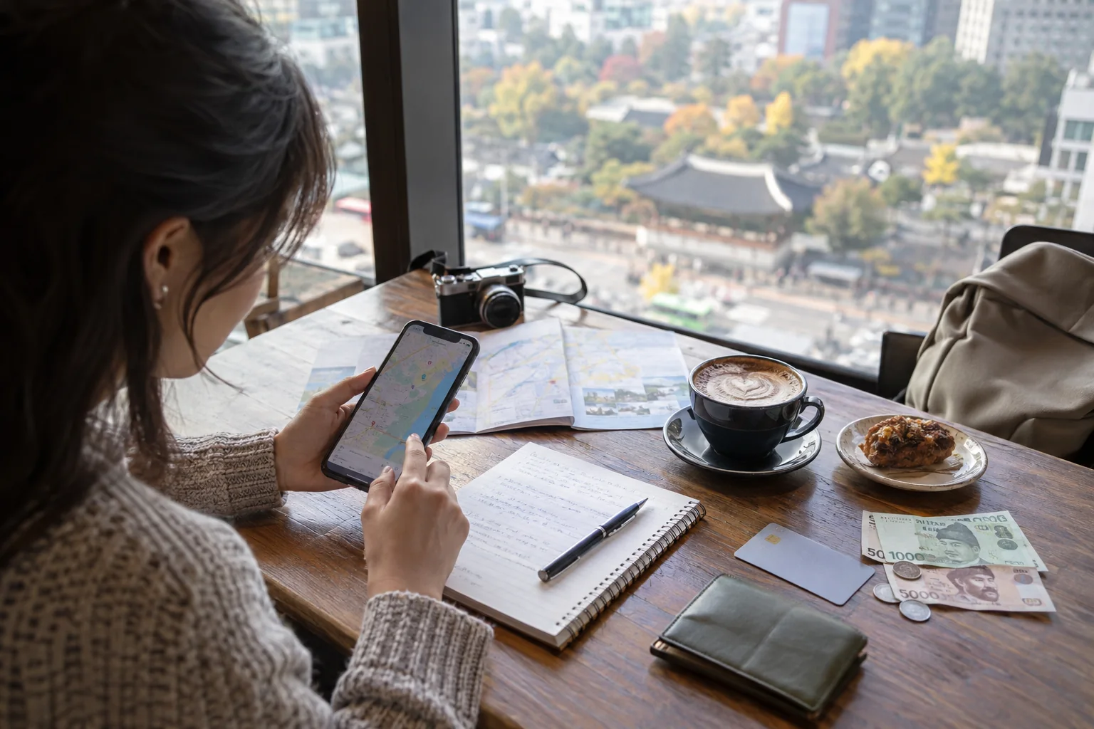 Traveler planning a Korea budget with a phone, notebook, wallet and Korean won at a cafe