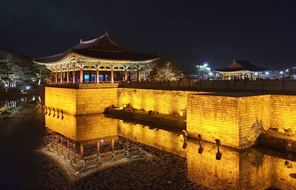 Illuminated Donggung Palace pavilions and stone embankment beside Wolji Pond at night